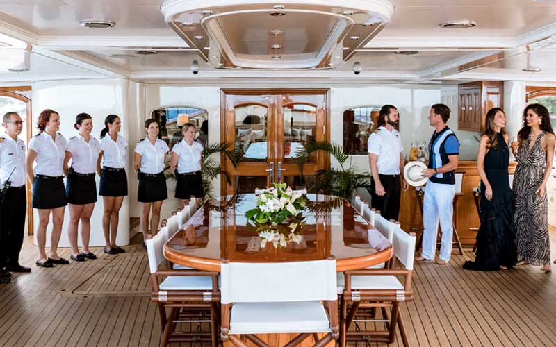A wooden dining table with 6 members of NERO's crew to the left and one crewmember to the right socializing with 3 guests.