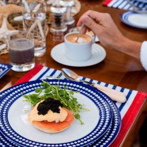Plate of salmon eggs benedict on a white and blue plate on NERO yacht. Hand is seen stirring a cup of coffee.