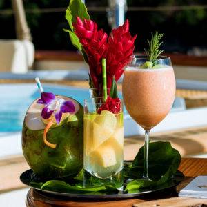 One drink in a coconut, another with chunks of fuit and a large red flower and a third frozen drink in a wine glass on NERO Yacht.