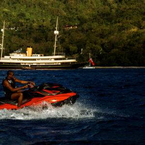 Man riding a red and black JetSki with Nero Yacht in the background.