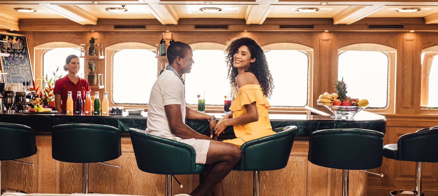 Man and woman sitting at the bar on NERO yacht with bartender off to the corner smiling at couple.