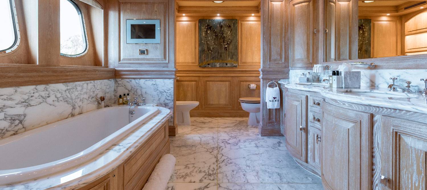 Bathtub in NERO Yacht master suite surrounded by white and black swirrled marble, a dual-sink vanity, toilet and a bidet